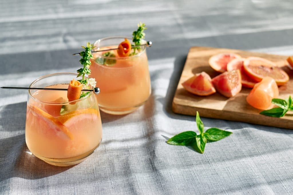 Summer refreshing grapefruit drink or alcoholic cocktail with grapefruit slices, ice and herbs.